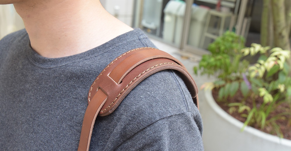 職人手作咖啡色皮革肩墊，搭配縫線細節，裝戴於灰色T恤的肩膀上。