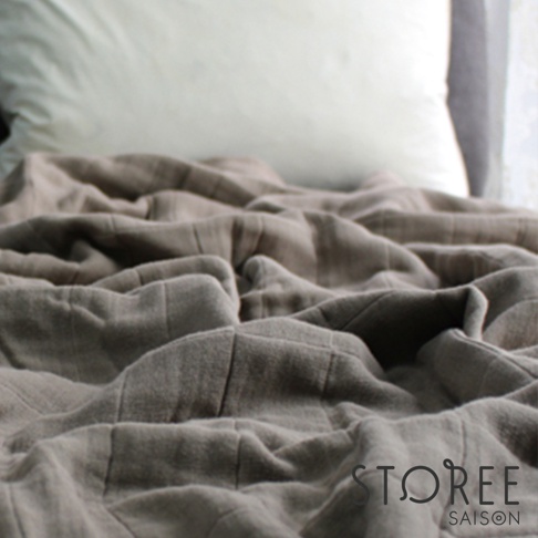 九層紗單人毯，呈現柔軟的褶皺，材質輕薄，顏色為柔和的灰褐色。