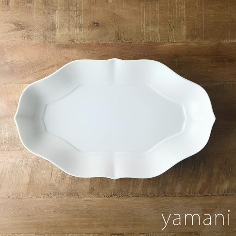 淡青白釉美濃燒輪花長盤，以陶瓷製成，呈現柔和的白色調，盤緣帶有輪狀花瓣紋飾，中央有八角形凹槽，置於木紋背景上。