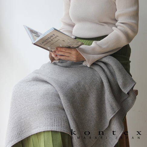 一件淺灰色針織風純棉浴巾，質地柔軟，呈現自然垂墜感，搭配米白色羅紋針織上衣及綠色褶裙。