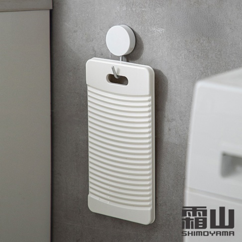 日本製白色輕便型迷你洗衣板，表面有橫向條紋設計，頂部有掛孔，透過掛鉤懸掛在灰色牆面上。