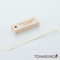 淺色木紋檜木塊，表面蝕刻有「Natural Hinoki Block TONARINO」字樣及圖示，一旁擺放著一條米白色織帶。