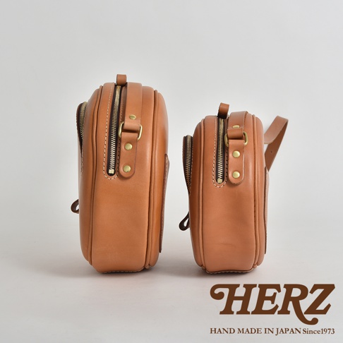 兩個棕褐色皮革小圓包，一個較大，一個較小，側面特寫，展示其材質、縫線及黃銅拉鍊。