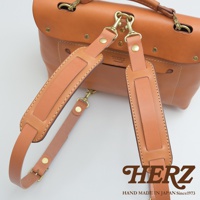 職人手作皮革肩墊，使用淺棕色皮革製作，附有黃銅色金屬扣環，可連接至包包。肩墊設計精緻，縫線清晰，展現職人細膩工藝。