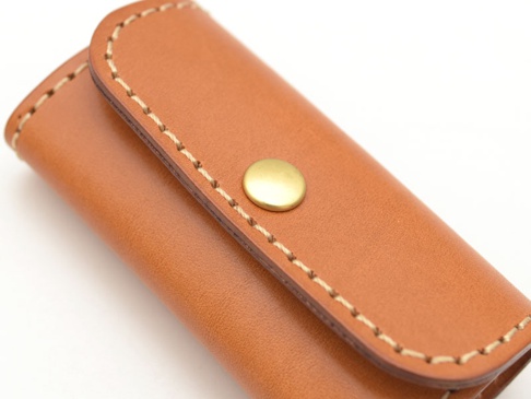 棕色皮革鑰匙包，帶有四個金屬鉤和一個黃銅按扣。包身採用手工縫線，材質為真皮。