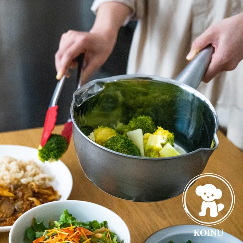 一個三層不鏽鋼雪平鍋，鍋內裝有綠色西蘭花和黃色塊狀物。一隻手使用紅色夾子夾起一塊西蘭花，鍋柄朝向右側。