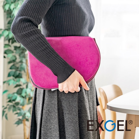 帶有精緻絨面質感的桃紅色進階款隨身坐墊，邊緣有黑色滾邊，由一位身穿黑色羅紋上衣和灰色裙子的女士手持。