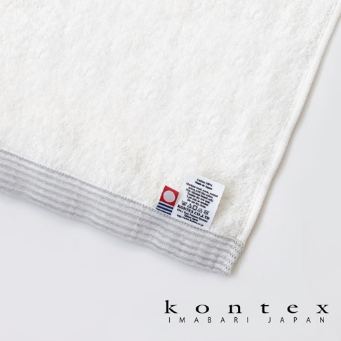 今治純棉浴巾，白色主體，帶有灰色細條紋邊緣，材質標籤標示為「Cotton 100% Made in Japan」。