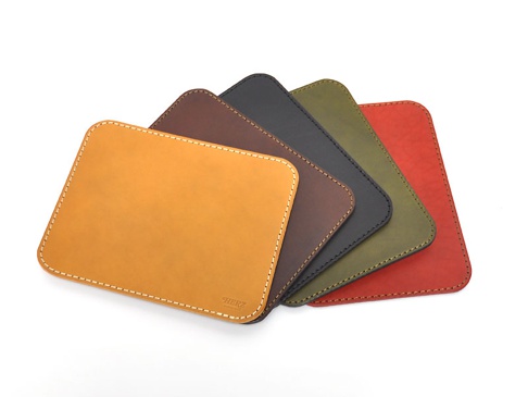 五款職人手作皮革滑鼠墊板，分別為黃褐色、深棕色、炭黑色、橄欖綠和紅色，皆為方形帶圓角的設計，邊緣以對比色縫線處理，質感細膩。