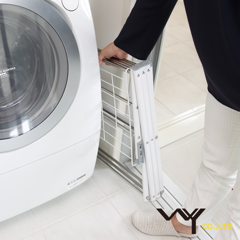 一位女士正在將一個可折疊的白色菱形晾曬架靠在洗衣機旁。