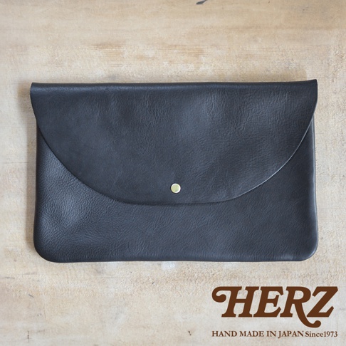 黑色皮革製成、鈕扣式封口、簡約設計的小物收納袋，置於木紋背景上。