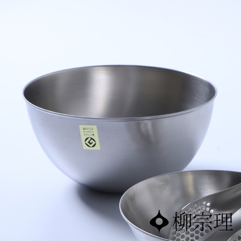 一個不鏽鋼調理盆，直徑 23 公分，盆身光滑，帶有日文標籤，盆旁另有一個較小的同材質調理盆，內有漏勺。
