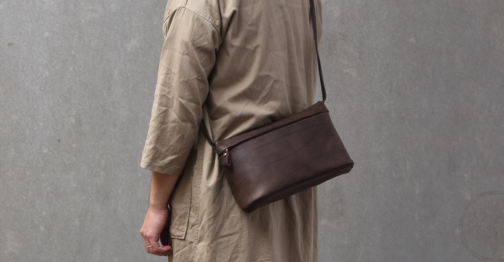 一個棕色皮革斜背包，搭配米色長袖上衣，斜掛在模特兒身上。