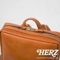 職人手作皮革軟皮商務後背包，近拍展示包款頂部皮革材質、縫線細節，以及金色雙拉鍊和皮革提把。