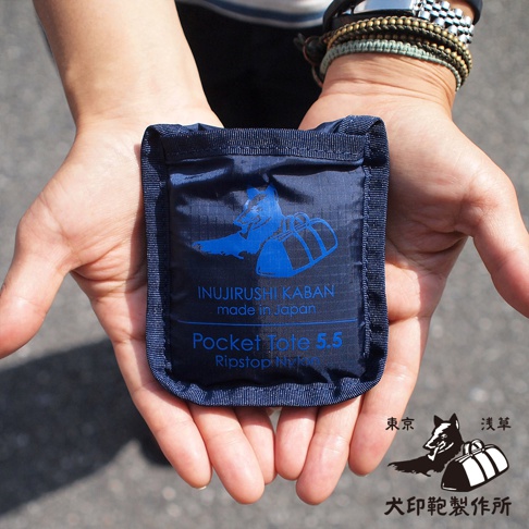 深藍色犬印鞄環保折疊收納購物袋，採用Ripstop Nylon材質，袋面印有狗與行李箱的藍色圖案及品牌標誌。