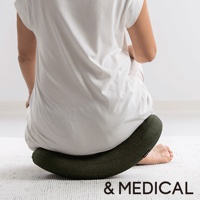 綠色U型搖搖枕，表面織紋清晰，置於白色地毯上，一位穿著白色上衣、米色褲子的人盤腿坐於其上。