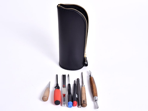 黑色皮革直立式筆袋，搭配金色拉鍊，旁邊擺放著多款不同尺寸的工具，包括螺絲起子、削皮刀及雕刻刀等，整體呈現簡約專業感。