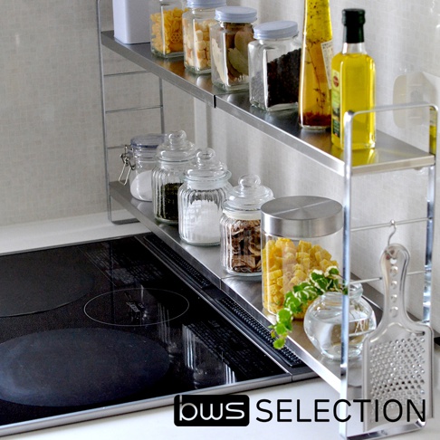 不鏽鋼可伸縮雙層收納架，兩層架上擺放多種玻璃罐裝食材，如義大利麵、香料、橄欖油等。架子旁有一個不鏽鋼磨泥器，以及一個掛著三個S型掛勾的支架。