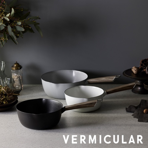 桌面展示著三個不同顏色的 Vermicular 琺瑯鑄鐵雪平鍋，分別為黑、白與淺灰色，皆配有優雅的木質把手，放置在簡約的深色背景與灰色檯面上，下方並印有 Vermicular 品牌名稱。