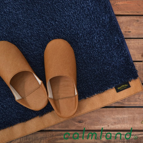 深藍色毛圈織物玄關地墊，搭配一雙棕色皮革室內拖鞋，地墊邊緣有棕色滾邊，角落有Ward Robe品牌標籤。