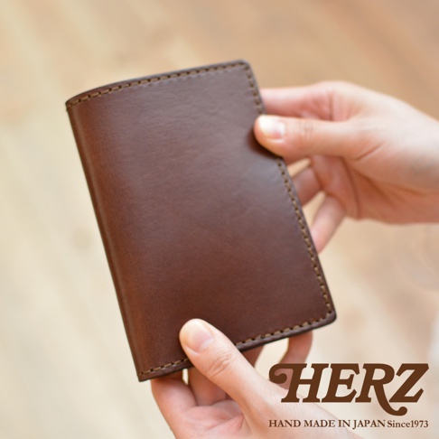 職人手作皮革經典護照套，深棕色皮革，細緻車縫線，雙手拿著展示。