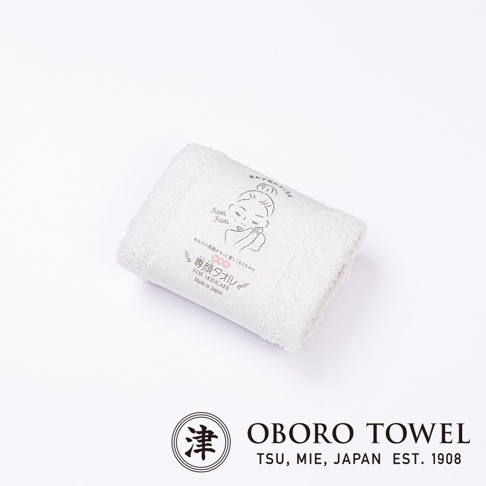 一條白色純棉專用洗臉毛巾平放在純白背景上，中間包裹著印有女性插畫與日文字樣的紙質腰封，圖片下方標示著日本 Oboro Towel 津市品牌與成立年份。