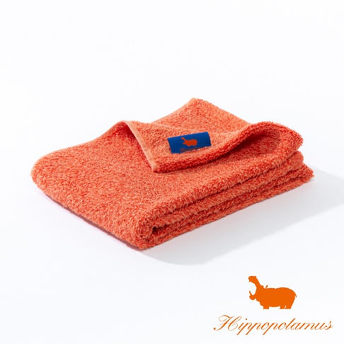 疊放的珊瑚色竹棉混紡長毛巾，表面有橙色河馬標誌的藍色織標。