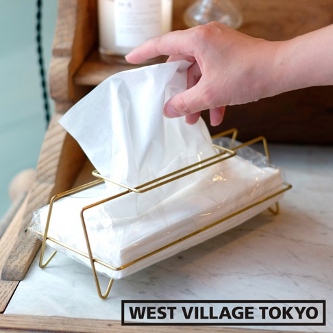 黃銅色金屬線條構成的長方形面紙盒，內含多包白色面紙，一隻手正從盒中抽取一張面紙。