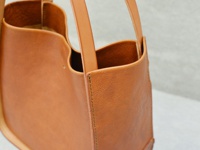 棕褐色皮革製的方形托特包，質感細緻，兩個肩帶從包身延伸而出，包口結構略有彎曲，整體呈現簡約的設計風格。