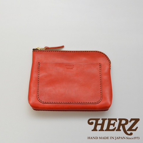 橘紅色職人手作皮革小物收納包，配有金色拉鍊，正面有一個方形插袋，邊緣縫線精緻，展現皮革的自然紋理。