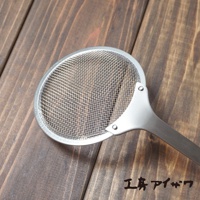 不鏽鋼萬用撈油勺，帶有細緻網孔的圓形濾網，連接至一體成形的不鏽鋼手柄，整體呈現銀色金屬光澤，放置於深棕色木紋背景上。