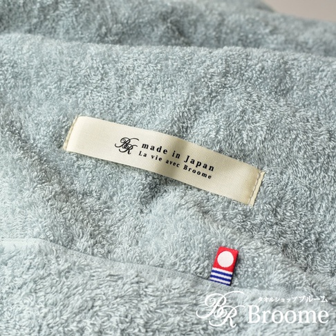 淺藍色今治毛巾被，觸感柔軟，帶有「made in Japan」和「La vie avec Broome」字樣的米白色標籤，以及一個帶有圓點和藍白條紋的紅色小標誌。