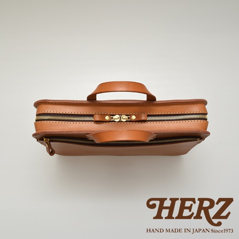 職人手作皮革兩用商務公事包，採用天然皮革材質，呈現溫潤的棕褐色調，配有雙拉鍊開合及頂部提把，簡約俐落的設計。