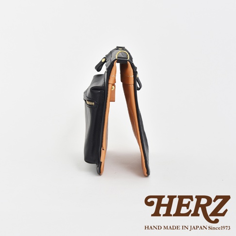 職人手作皮革翻轉雙色直式斜背包，外層為黑色皮革，內裡為棕色皮革，設有拉鍊開口及金屬扣環。