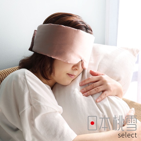 一位女性戴著粉藕色絲綢眼罩，雙手擁抱白色柔軟抱枕，神情放鬆地休息，右下角印有日本桃雪 select 的品牌標誌。