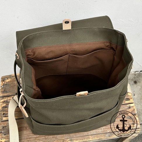 loiter 高島帆布前蓋式背包，軍綠色帆布材質，內部有深棕色襯裡及多個隔層，前側有兩個外袋，肩帶為米白色帆布，搭配皮革束帶和金屬扣。