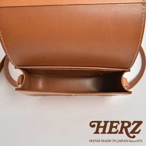 職人手作皮革翻蓋橫式單肩包，採用天然皮革製作，呈現溫潤的棕褐色。包款設計簡約，翻蓋處縫線清晰，內部空間一覽無遺，展現皮革的細緻質感。