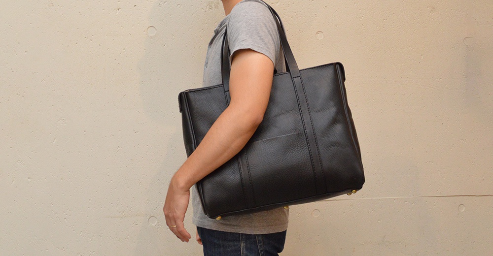 黑色皮革托特包，具有拉鍊開合和肩背帶，包身有縫線細節和外部口袋。