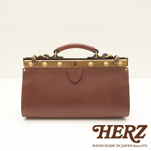 棕色皮革製成的復古口金兩用手提包，帶有金色金屬配件和提把。包包正面有盾牌形狀的皮革裝飾，整體呈現簡約經典的風格。