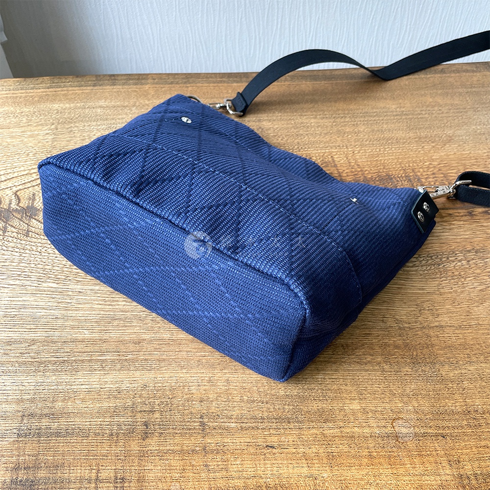 深藍色刺子織迷你側背包，織紋呈現菱格與直線交織，配有黑色織帶與銀色金屬扣環。