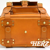 棕色皮革製成的職人手作旅行後背包，綴有金色金屬扣環與鉚釘，展現復古風格。