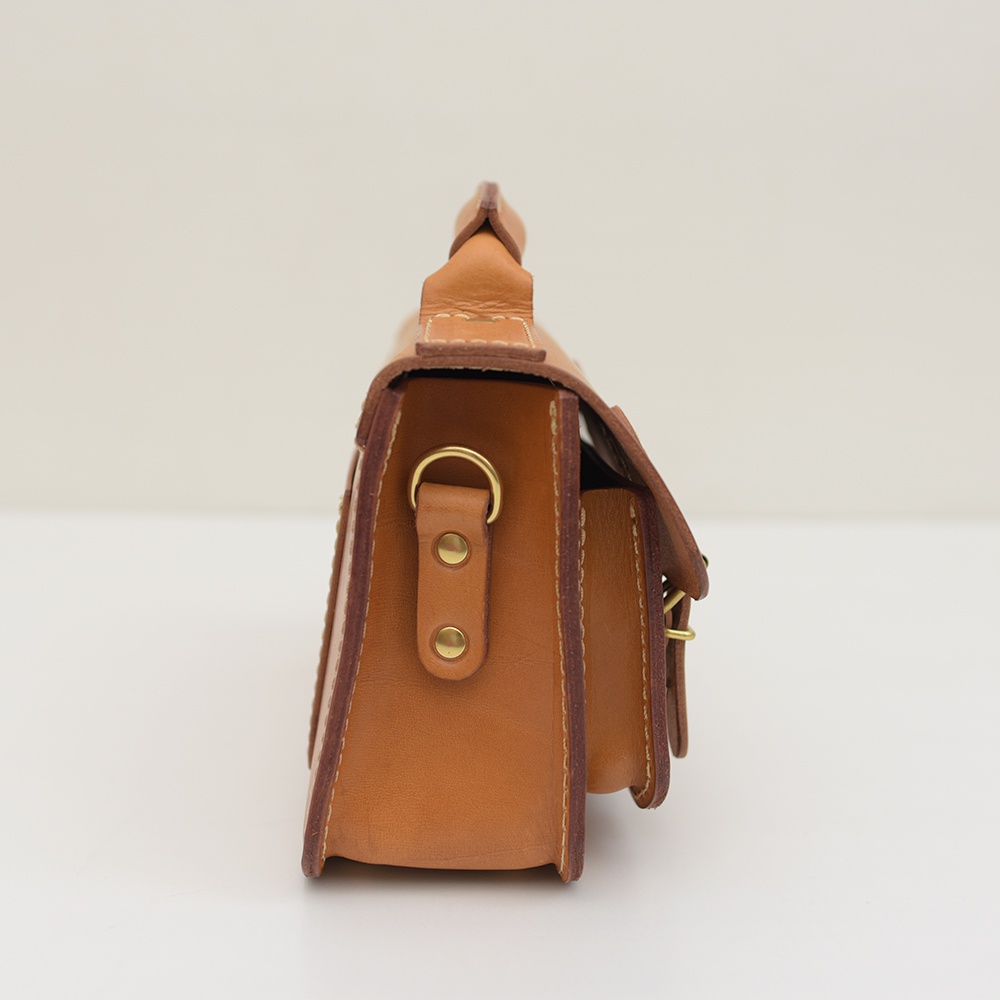 棕色皮革迷你肩背包，側邊視角，有雙扣設計與金色五金配件。