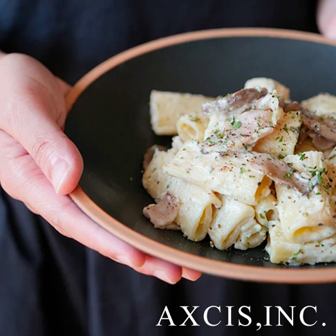 手持黑色素燒陶瓷義大利麵盤，盤中盛滿奶油白醬雞肉義大利麵，撒有綠色香草與黑胡椒。