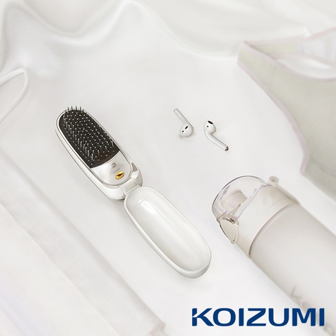 白色充電式負離子音波磁氣美髮梳，梳齒為黑色，梳柄與梳蓋為白色，置於白色絲綢布料上，旁有無線耳機與白色保溫瓶。