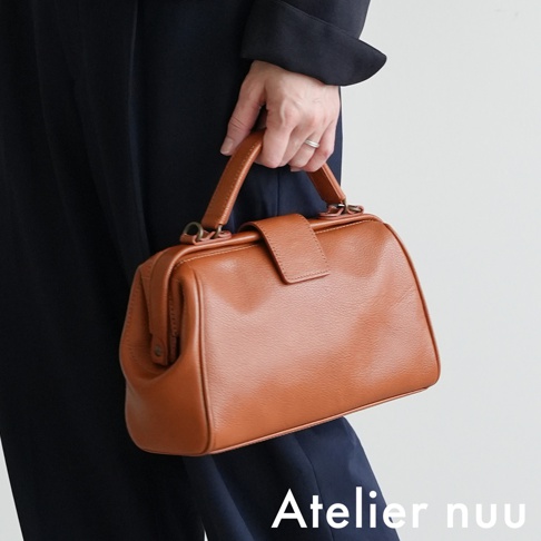 Atelier nuu 棕色皮革小款手提包，搭配黑色衣物，展現經典風格。