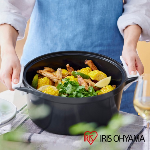 IRIS OHYAMA 萬用無水調理鍋內盛放著香氣四溢的雞翅玉米料理，鍋身為黑色，旁邊擺放著一杯香檳，整體呈現出美味的烹飪畫面。