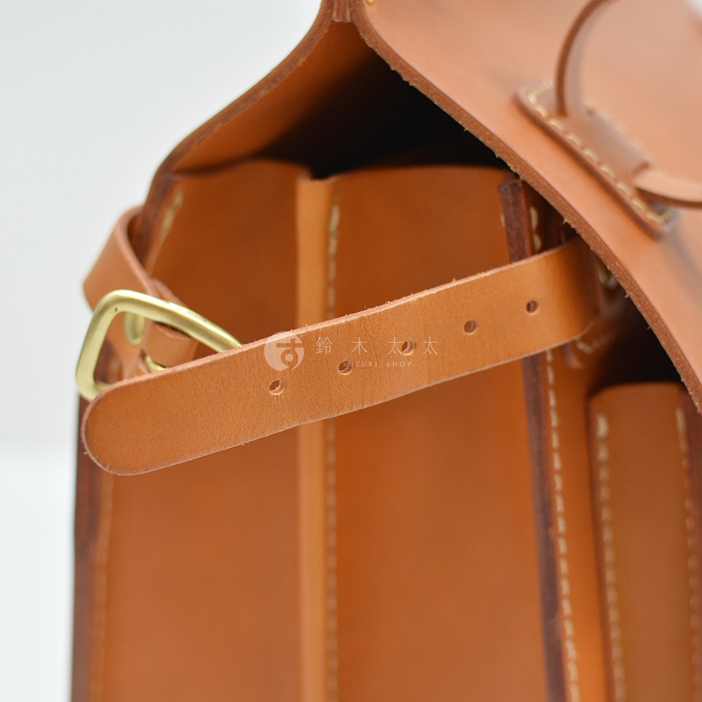 職人手作皮革旅行包 A-102 採用天然皮革製成，呈現溫潤的焦糖棕色。包身結構清晰，搭配黃銅色金屬釦環與多個調整孔的皮革背帶，展現細緻的手工藝。