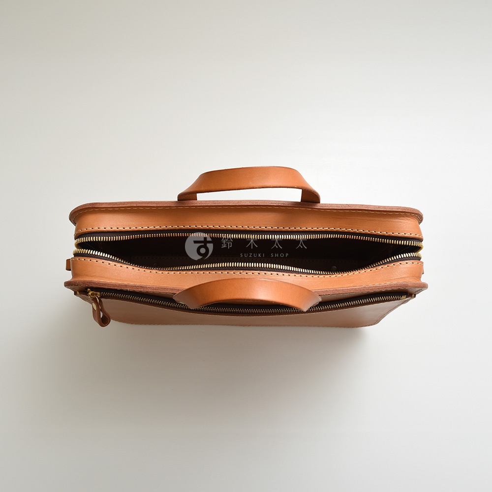 職人手作的棕色皮革兩用商務公事包，頂部有提把，側邊有拉鍊開口，內部可見品牌標誌。