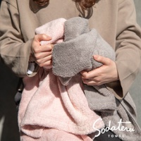 雙手捧著兩條蓬鬆柔軟的毛巾，一條為柔和的粉紅色，另一條為淺灰色。毛巾材質看起來輕盈，觸感細膩。