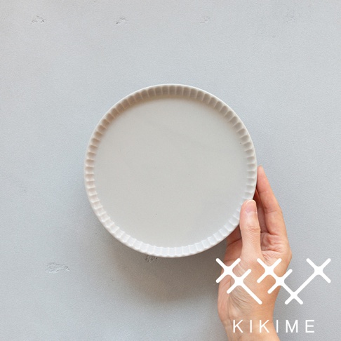 一只手拿著一個淺灰色的美濃燒高腳平盤，盤緣帶有放射狀的紋理。